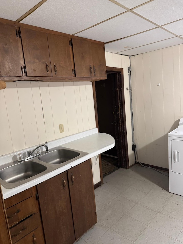 kitchen featuring washer / dryer, dark brown cabinets, wood walls, and sink