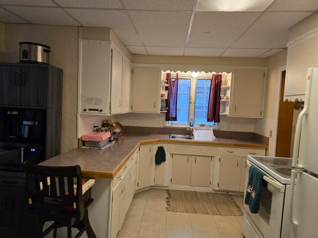 kitchen featuring a paneled ceiling, white appliances, white cabinets, sink, and light tile patterned flooring