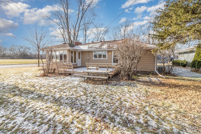 snow covered rear of property featuring a sunroom and a wooden deck