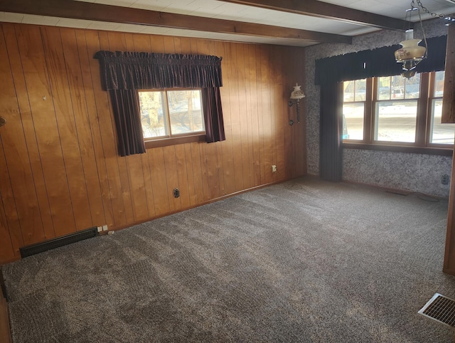 empty room with visible vents, beam ceiling, wooden walls, and carpet flooring