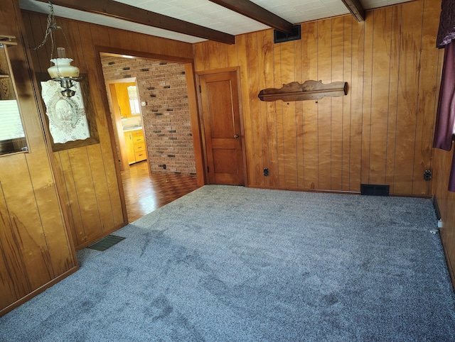 carpeted spare room with beamed ceiling, wooden walls, and visible vents