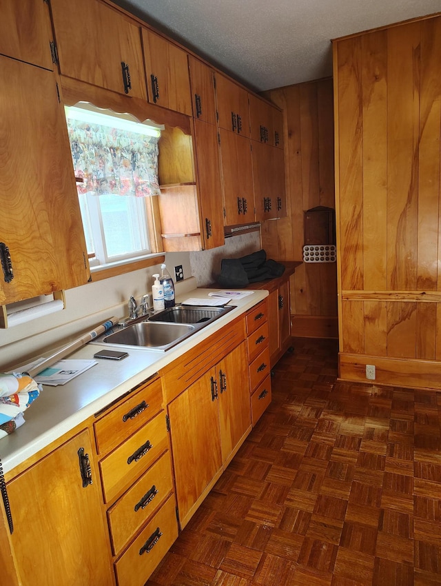 kitchen with a sink, light countertops, wood walls, a textured ceiling, and brown cabinets