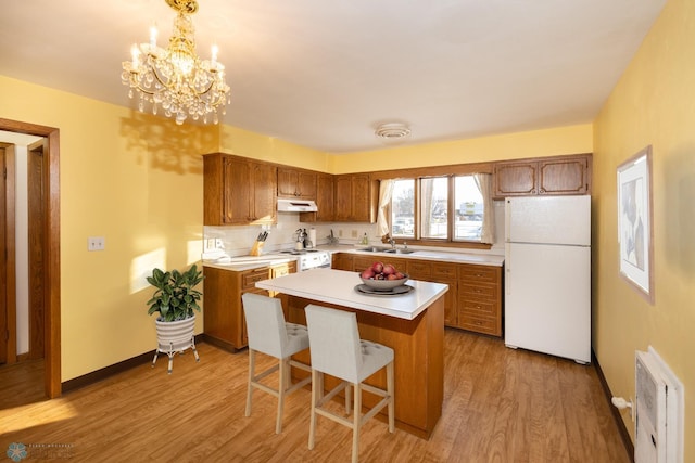 kitchen with a chandelier, decorative light fixtures, white appliances, a kitchen island, and light wood-type flooring