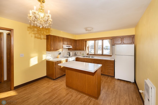 kitchen with white appliances, an inviting chandelier, hanging light fixtures, light wood-type flooring, and a kitchen island