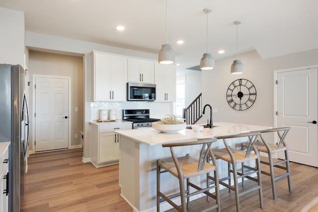 kitchen featuring appliances with stainless steel finishes, a kitchen island with sink, pendant lighting, light hardwood / wood-style flooring, and white cabinets