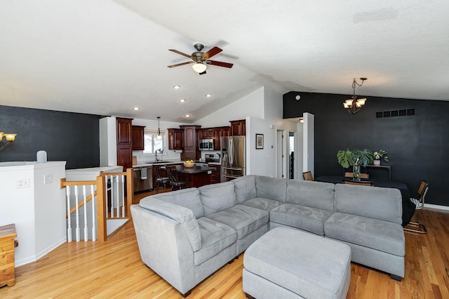 living room with visible vents, light wood finished floors, baseboards, lofted ceiling, and ceiling fan with notable chandelier