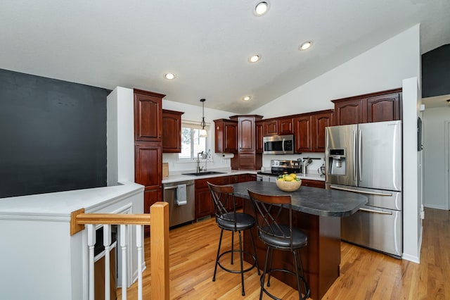 kitchen with a breakfast bar, light wood-style flooring, a sink, stainless steel appliances, and vaulted ceiling