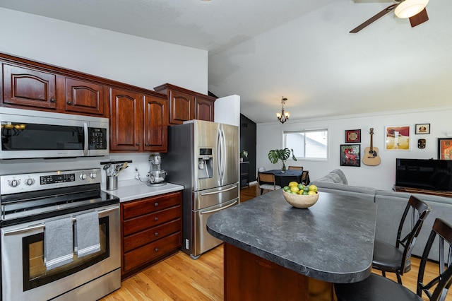 kitchen featuring light wood finished floors, lofted ceiling, stainless steel appliances, a kitchen bar, and open floor plan