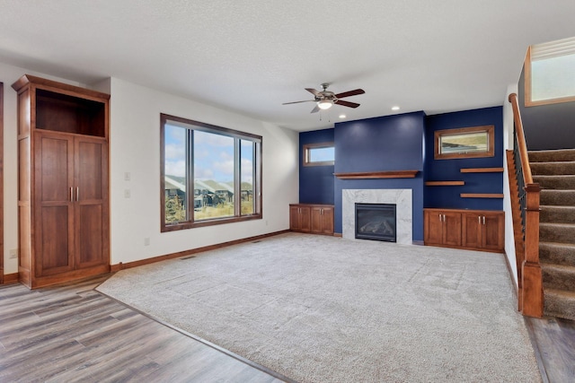 unfurnished living room featuring ceiling fan, a high end fireplace, a textured ceiling, and light wood-type flooring