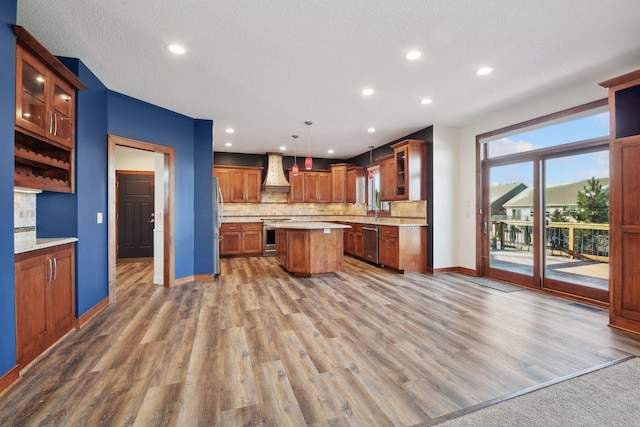 kitchen featuring premium range hood, tasteful backsplash, pendant lighting, wood-type flooring, and a center island