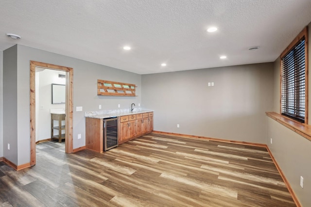 bar with light stone countertops, a textured ceiling, dark wood-type flooring, sink, and wine cooler