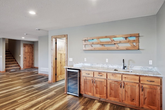 bar with light stone countertops, a textured ceiling, beverage cooler, dark wood-type flooring, and sink