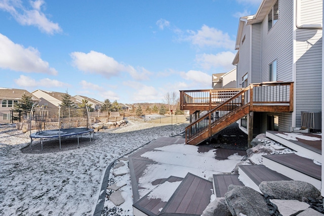 yard layered in snow featuring a wooden deck and a trampoline