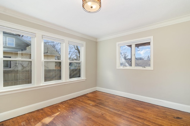 empty room with crown molding, plenty of natural light, hardwood / wood-style flooring, and baseboards