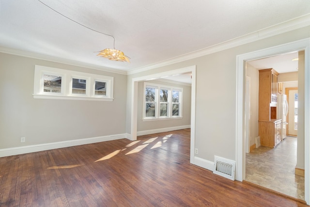 empty room with baseboards, crown molding, visible vents, and hardwood / wood-style floors