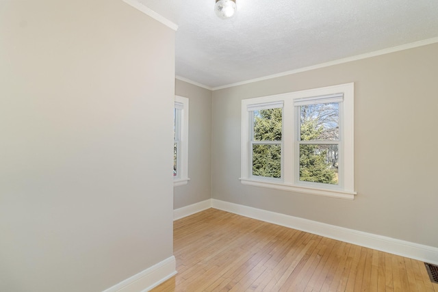 spare room with a textured ceiling, ornamental molding, light wood-type flooring, and baseboards