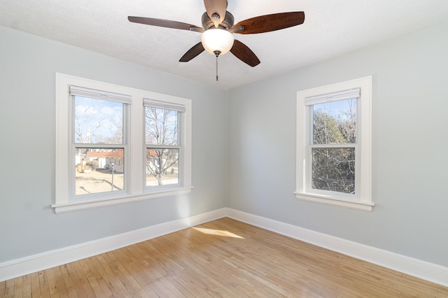 empty room with light wood-type flooring, baseboards, and a textured ceiling