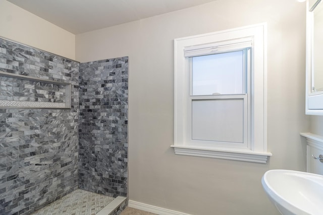 bathroom featuring a sink, a tile shower, and baseboards