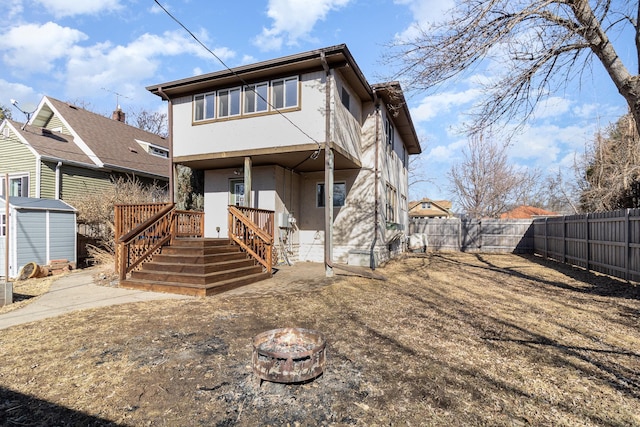 rear view of property with an outbuilding, an outdoor fire pit, a fenced backyard, and stucco siding