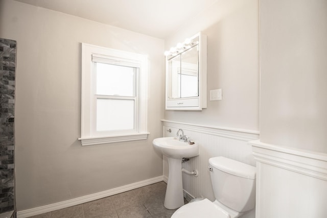 bathroom with tile patterned flooring, toilet, a sink, wainscoting, and a tile shower