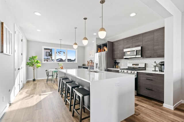 kitchen with stainless steel appliances, dark brown cabinets, light countertops, and a center island with sink