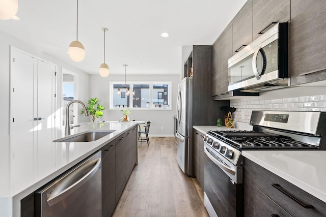 kitchen with stainless steel appliances, light countertops, a sink, and decorative light fixtures