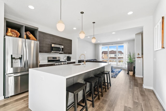 kitchen featuring appliances with stainless steel finishes, a breakfast bar area, a kitchen island with sink, light countertops, and a sink