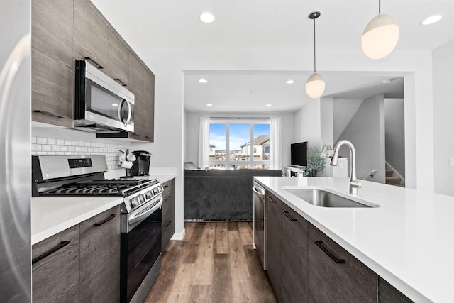 kitchen with a sink, light countertops, appliances with stainless steel finishes, dark wood finished floors, and pendant lighting