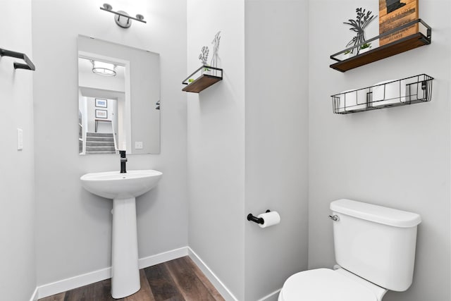 half bath with toilet, baseboards, and wood finished floors