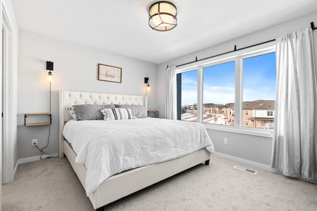 bedroom with light carpet, a textured ceiling, visible vents, and baseboards