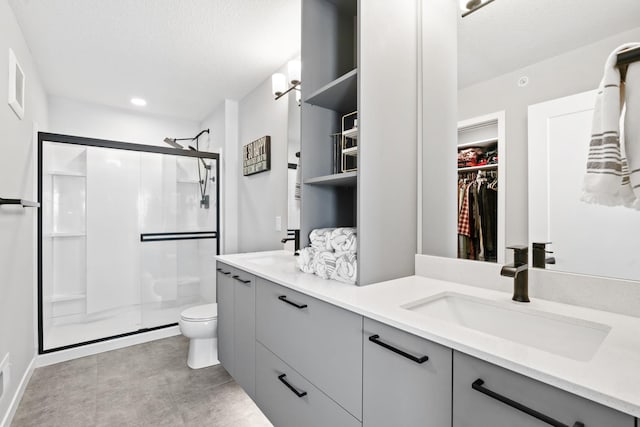 full bathroom featuring double vanity, a stall shower, toilet, a walk in closet, and a sink