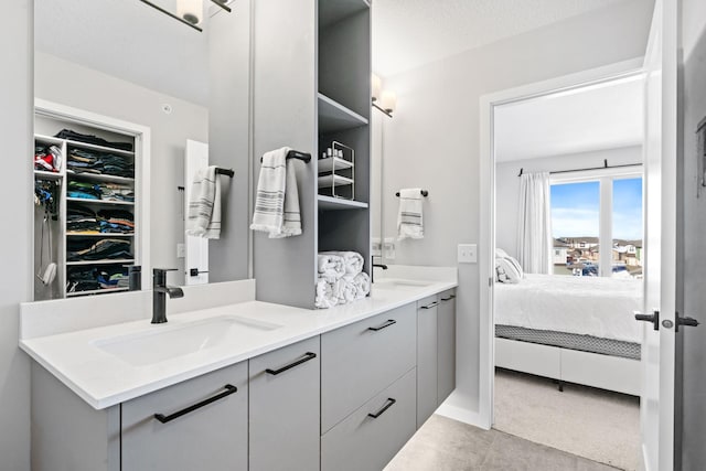 ensuite bathroom with ensuite bathroom, a textured ceiling, a sink, double vanity, and a walk in closet