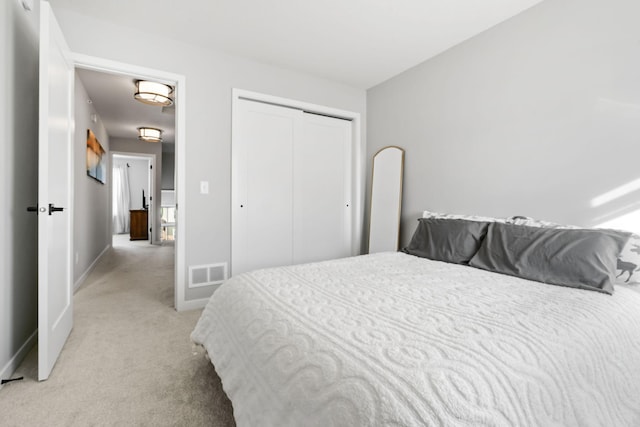 bedroom with a closet, visible vents, light carpet, and baseboards