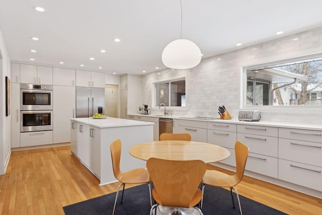 kitchen with appliances with stainless steel finishes, pendant lighting, white cabinetry, a center island, and light hardwood / wood-style floors