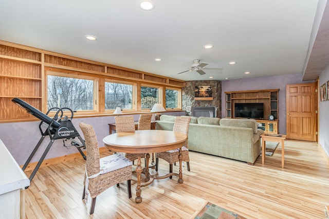 dining area with light wood-type flooring, a stone fireplace, and ceiling fan