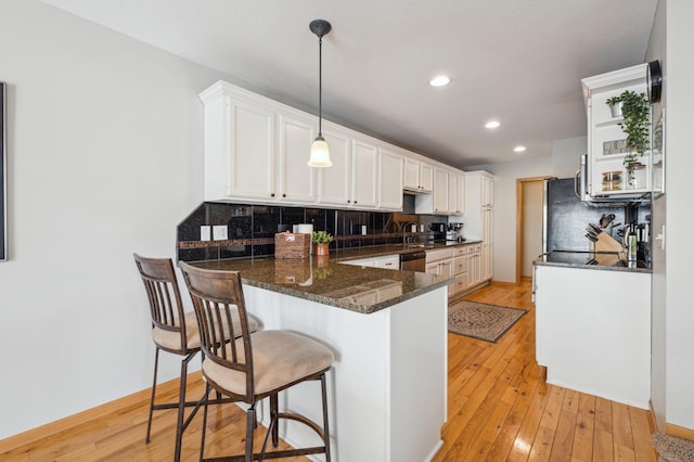 kitchen featuring decorative light fixtures, white cabinetry, backsplash, kitchen peninsula, and light wood-type flooring