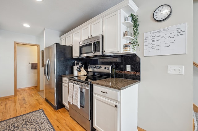 kitchen featuring light hardwood / wood-style flooring, dark stone countertops, white cabinets, stainless steel appliances, and backsplash