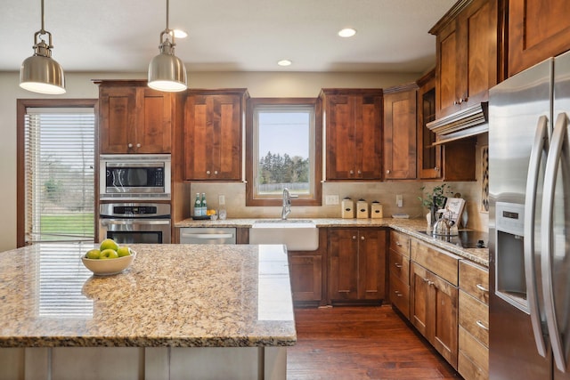 kitchen with light stone counters, stainless steel appliances, sink, dark hardwood / wood-style floors, and hanging light fixtures