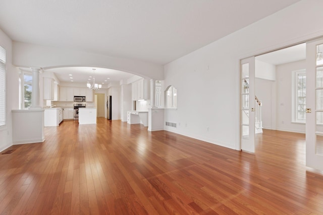 unfurnished living room featuring a wealth of natural light, light hardwood / wood-style floors, and a notable chandelier