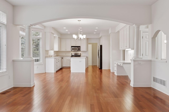 kitchen featuring hanging light fixtures, white cabinets, stainless steel appliances, and wood-type flooring