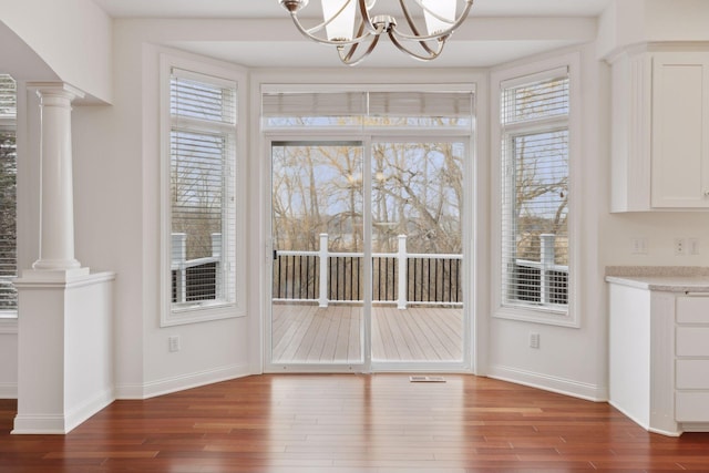 unfurnished dining area with a notable chandelier, dark hardwood / wood-style floors, and decorative columns