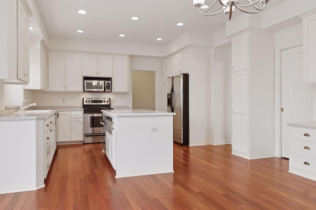 kitchen featuring stainless steel appliances, an inviting chandelier, hardwood / wood-style floors, a center island, and white cabinetry