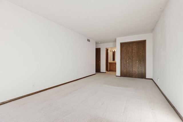 unfurnished bedroom with ensuite bath, light colored carpet, and a closet