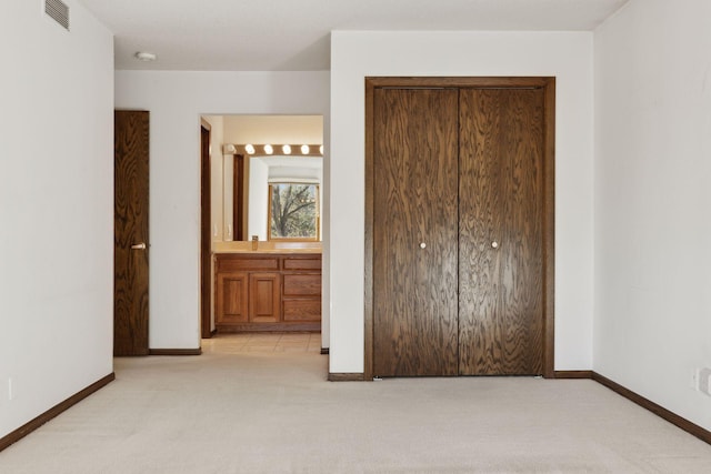 unfurnished bedroom with sink, light colored carpet, a closet, and ensuite bathroom