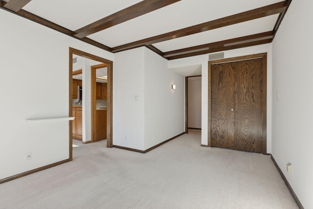 unfurnished bedroom with light carpet and beamed ceiling