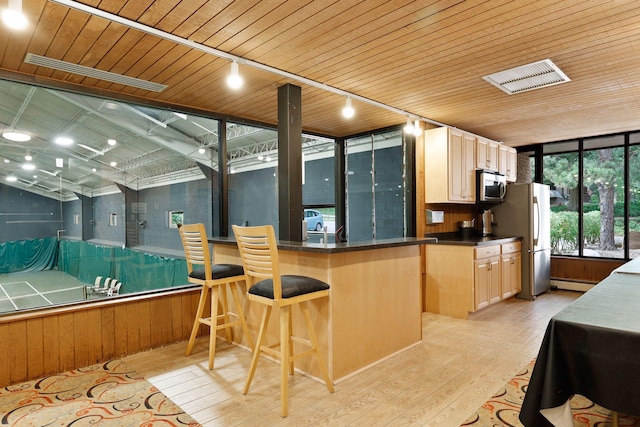 kitchen with a breakfast bar area, stainless steel appliances, light hardwood / wood-style floors, and wooden ceiling