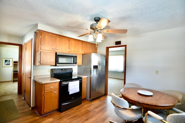 kitchen featuring ceiling fan, a textured ceiling, stainless steel appliances, and light hardwood / wood-style flooring