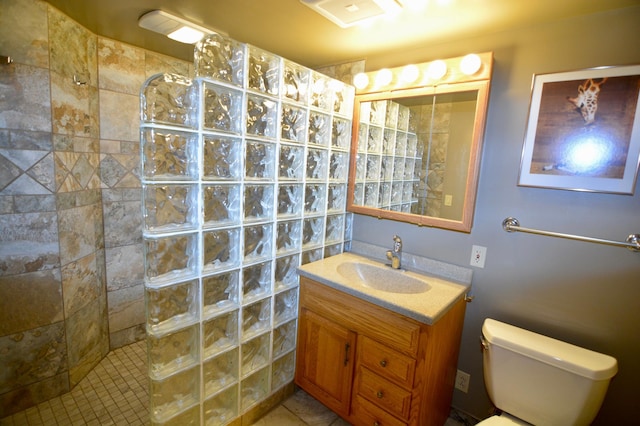 bathroom with toilet, tiled shower, and vanity