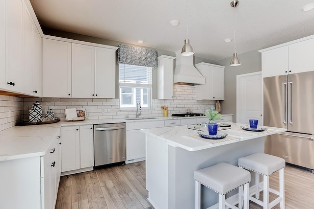 kitchen with a kitchen bar, custom range hood, a sink, appliances with stainless steel finishes, and light wood finished floors