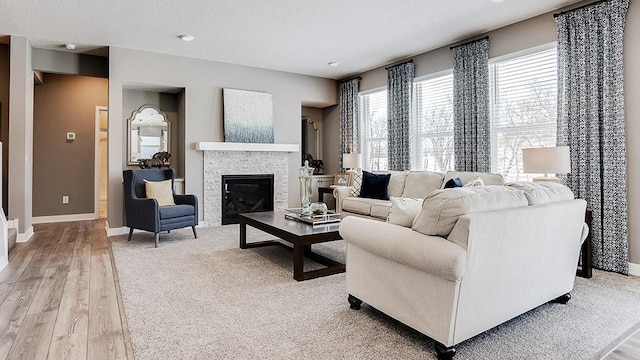 living area featuring light wood finished floors, a stone fireplace, a textured ceiling, and baseboards